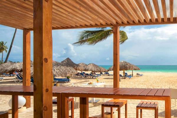 Außenbereich des Caribe Deluxe Princess Hotels mit Blick auf den Strand, Holzpavillons und weißen Stühlen.