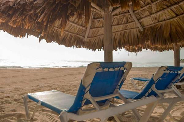 Strand mit Liegen unter Sonnenhut, das Caribe Deluxe Princess Hotel ist im Hintergrund zu sehen.