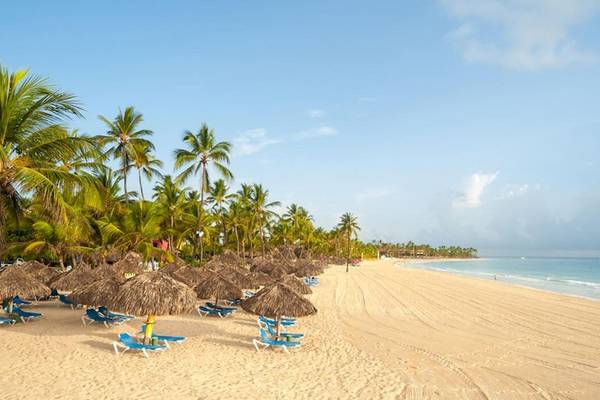 Strand des Caribe Deluxe Princess Hotels mit Palmen, Sonnenschirmen und Liegestühlen.