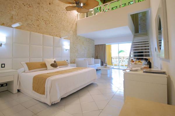 Ein modernes Hotelzimmer im Caribe Deluxe Princess Hotel mit weißem Bett, Sofa und Fliesenboden.