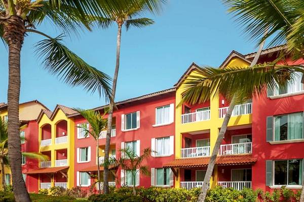Außenansicht des roten und gelben Caribe Deluxe Princess Hotels mit Palmen und Pflanzen davor.