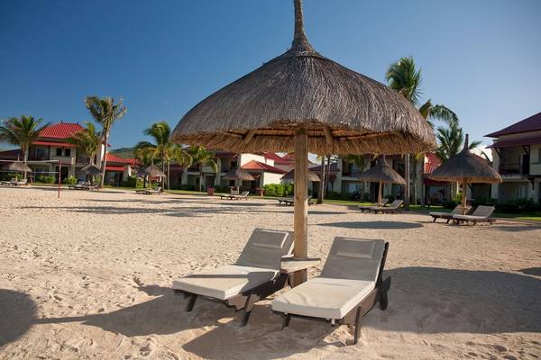 Strandszene des Tamassa Bel Ombre Hotels mit Sonnenliegen und Palmen im Hintergrund