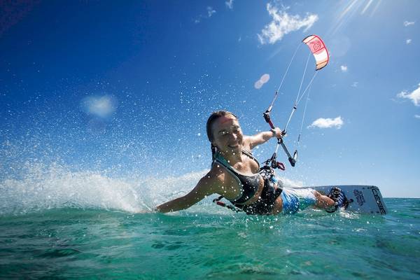 Eine Frau beim Kitesurfen im Ozean, strahlend lächelnd.