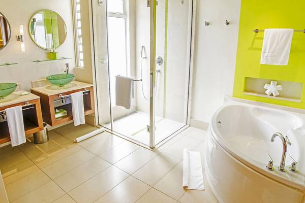 Badezimmer im Tamassa Bel Ombre Hotel mit zwei grünen Waschbecken, einer Duschkabine und einer Badewanne.