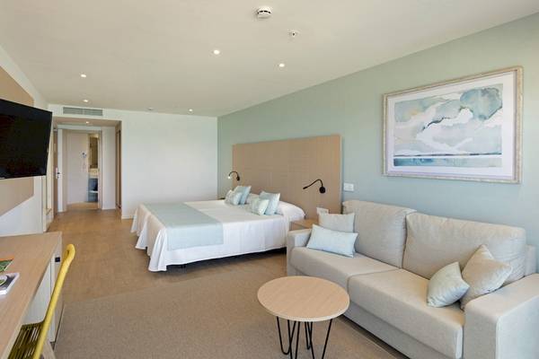 Innenansicht eines Zimmers im HSM Golden Playa Hotel mit Doppelbett, Sofa, Schreibtisch und Fernseher.