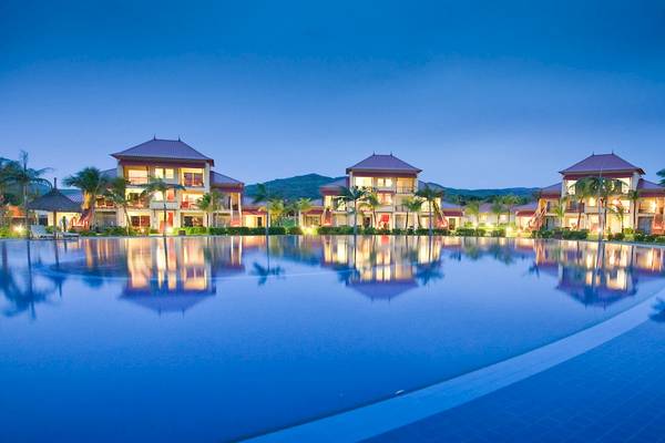 Nachtansicht des Tamassa Bel Ombre Hotels mit einem großen Pool, der die Gebäude widerspiegelt.