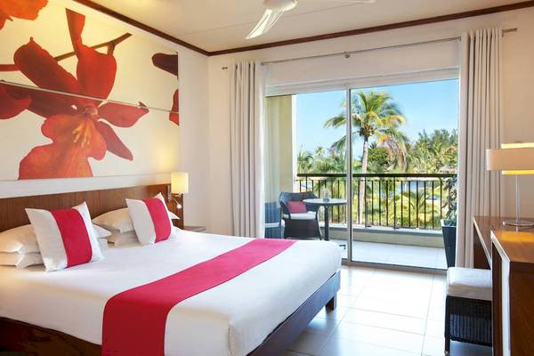 Ein Hotelzimmer im Tamassa Bel Ombre Hotel mit einem großen Bett und einem Balkon mit Blick auf die Palmen und das Meer.