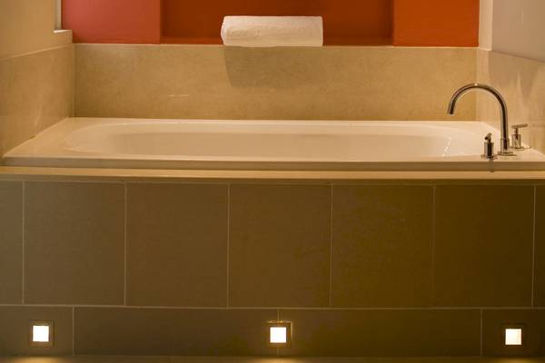 Badezimmer im Tamassa Bel Ombre Hotel mit Badewanne, Handtuchhalter und Beleuchtung.