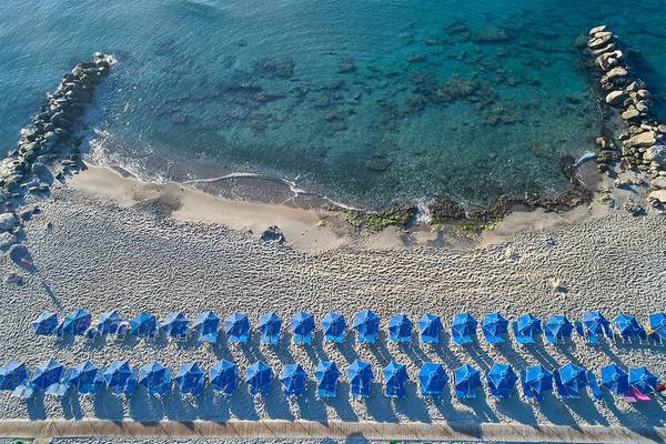 Luftaufnahme des Strandes des Porto Bello Royal Hotels mit blauen Sonnenhüten in einer Reihe.