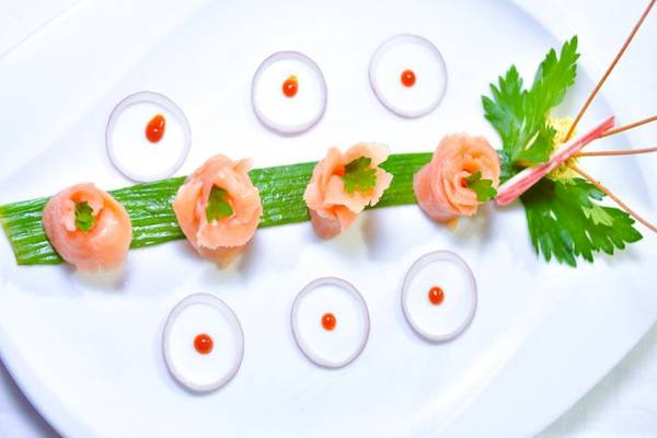 Fünf Stück roher Lachs auf einem Teller mit Zwiebelringen und Blattdekor