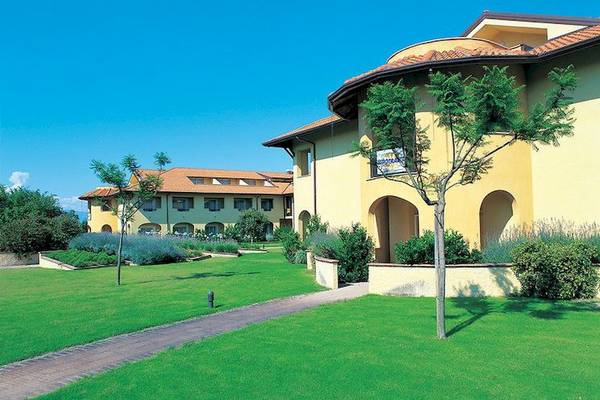 Außenansicht des Falkensteiner Club Funimation Garden Calabria Hotel, umgeben von Grünflächen und Bäumen.