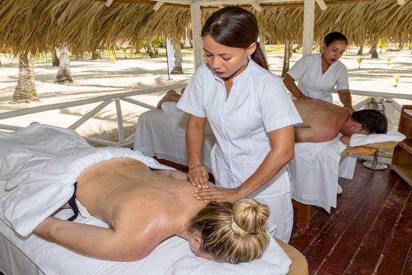 Massage im Spielplatz am Strand mit zwei Frauen, die Rückenmassagen an einem Mann und einer Frau durchführen.