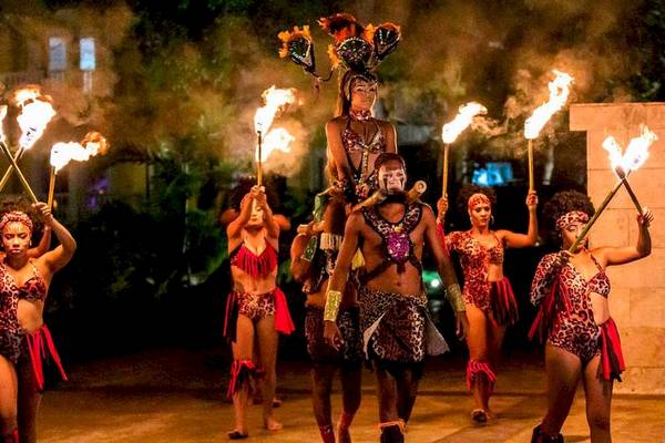 Gruppe von Tänzern in exotischen Kostümen führt eine Feuershow bei Nacht im Playabachata Spa Resort auf.