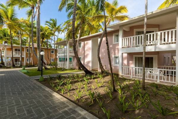 Außenansicht des Playabachata Spa Resorts mit pinken Gebäuden und Palmen im Hintergrund.