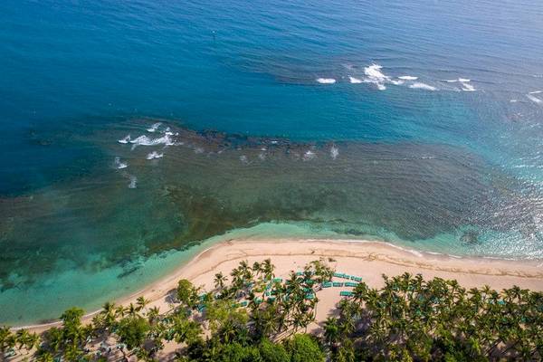 Luftaufnahme des Playabachata Spa Resorts Strand mit blauem Wasser und grünen Sonnenliegen.