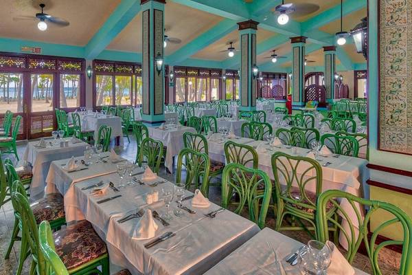 Innenansicht des Restaurants im Playabachata Spa Resort mit türkisblauen Wänden, weißen Tischen und grünen Stühlen, mit Blick auf den Strand.