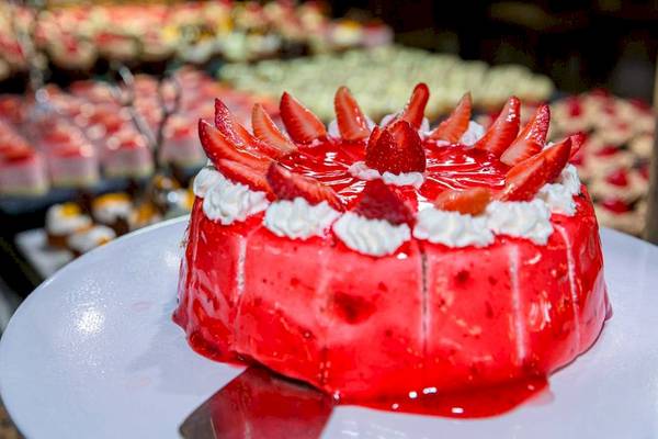 Ein roter Erdbeerkuchen auf einem weißen Teller im Hintergrund ein Buffet