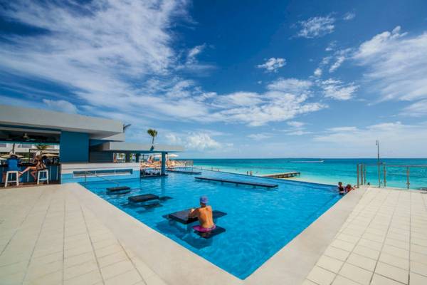 Außenpool des Riu Cancun Hotels mit einer Person im Schwimmbecken und mehreren Personen am Strand.
