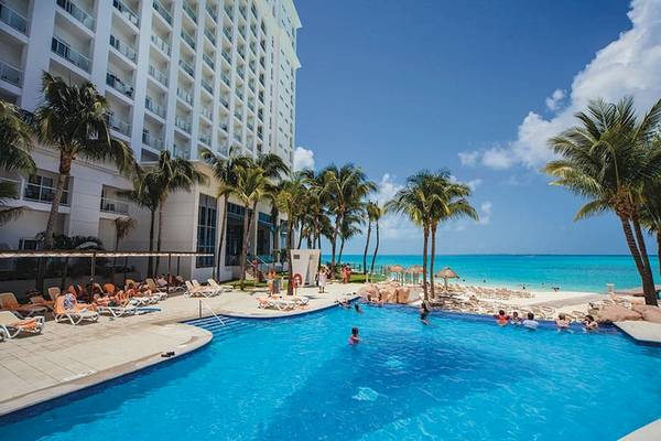 Außenpool des Riu Cancun Hotels mit vielen Gästen und Palmen im Hintergrund.
