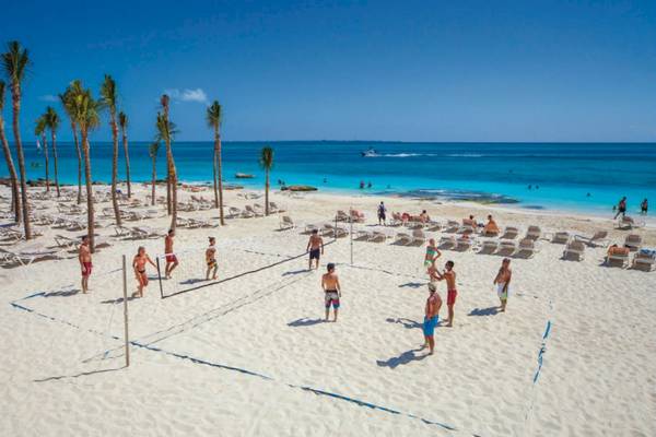 Volleyballspiel auf dem Strand des Riu Cancun Hotels mit Teilnehmern und Palmen im Hintergrund.