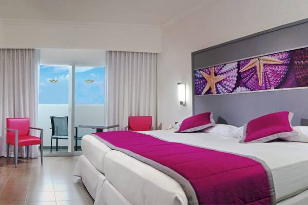 Hotelzimmer im Riu Cancun mit Doppelbett, zwei roten Stühlen und einem Tisch.