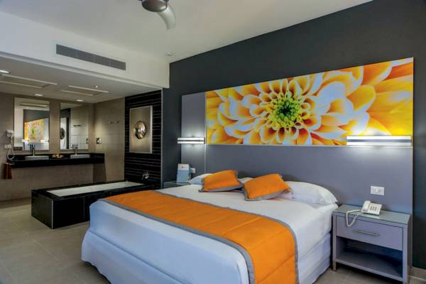 Innenansicht eines Zimmers im Riu Cancun Hotel mit Bett, Badewanne und Wandgemälde.