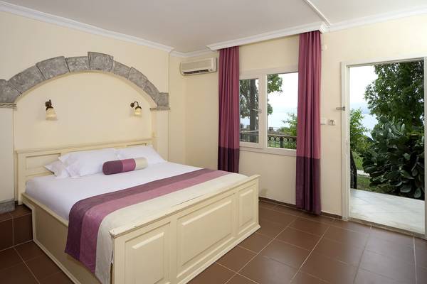 Schlafzimmer im Club Resort Atlantis mit einem Bett, Kissen und einem offenen Fenster, das einen Blick auf eine Terrasse und Bäume bietet.