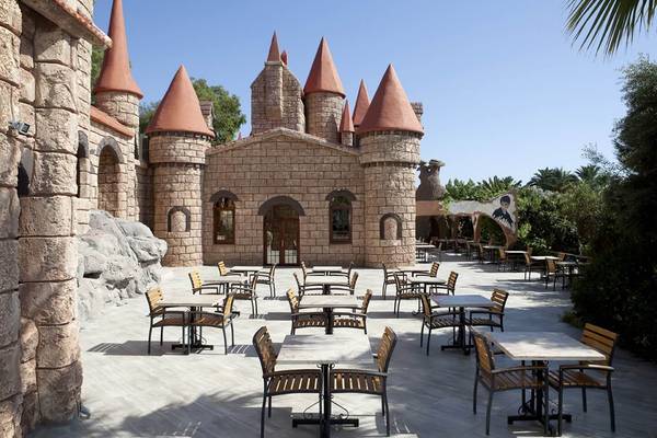 Außenbereich des Club Resort Atlantis mit runden Tischen und Stühlen vor einem burgartigen Gebäude.