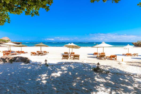 Strandszene im The Sands at Chale Island Resort mit weißen Sonnenschirmen und Holzliegen.