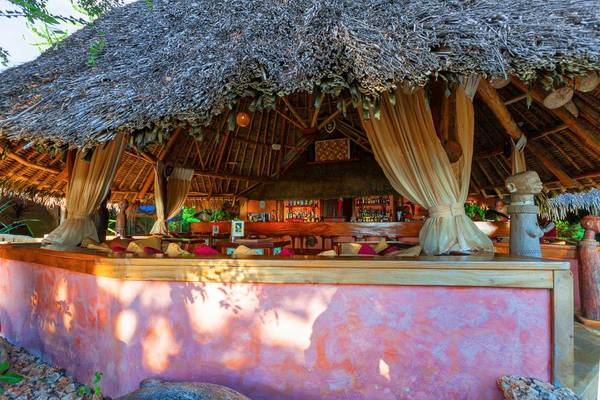 Die Bar im Sands at Chale Island Resort mit blauem Strohdach und rosa Wänden.