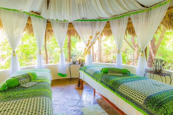 Spa-Behandlungsraum im Sands at Chale Island Resort mit zwei grünen und weißen Betten und großen Fenstern.
