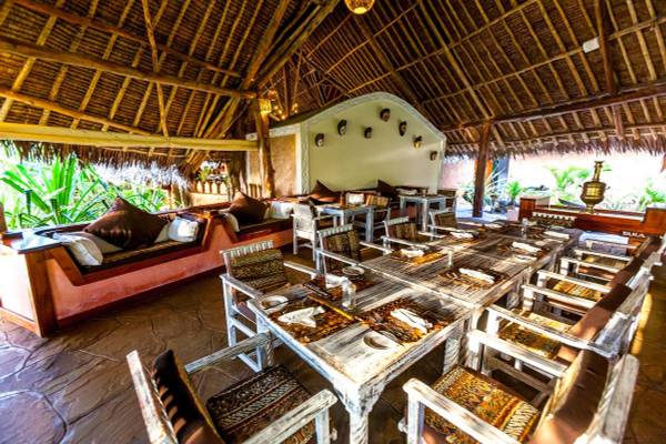 Innenbereich des Sands at Chale Island Resort mit runden Tischen, Stühlen und Kissen.