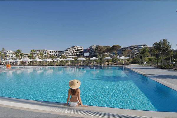 Ein Schwimmbad mit einer Frau, die am Rand sitzt, mit dem Susesi Luxury Resort im Hintergrund.