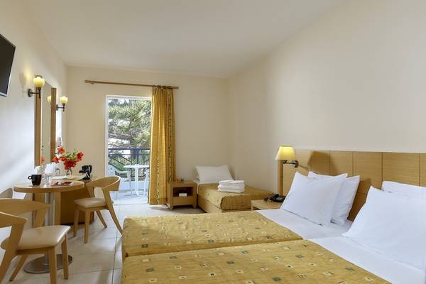 Doppelzimmer mit Balkon im Astir Beach Hotel auf Kreta, mit zwei Betten, einem Tisch und Stühlen, einem kleinen Nachttisch und einem Fernseher.