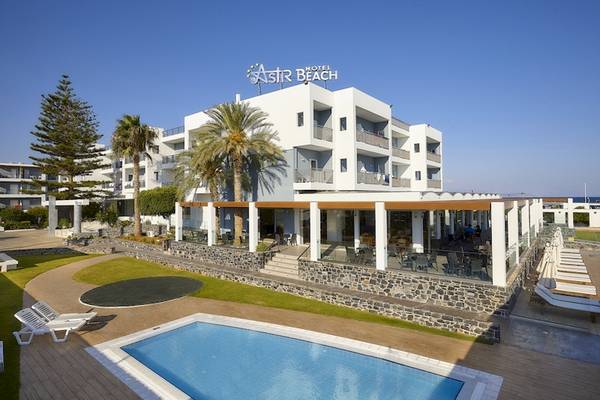 Außenansicht des Astir Beach Hotels auf Kreta mit Swimmingpool, Sonnenliegen und Palmen.