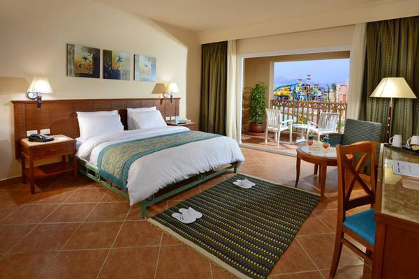 Charmillion Club Aqua Park Hotelzimmer mit Bett, Teppich, Schreibtisch und Balkon mit Wasserrutsche im Hintergrund.