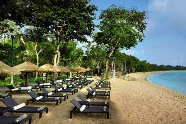 Außenbereich des Melia Bali Hotels mit Sonnenliegen, Palmen und einem Blick auf das Meer.