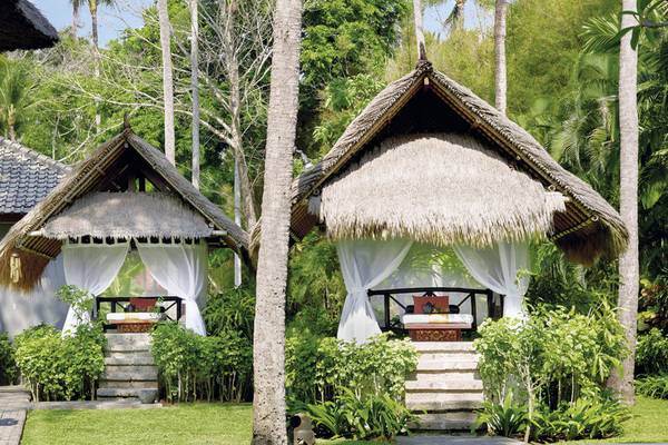 Zwei tropische Hütten des Melia Bali Hotels im Freien, umgeben von Pflanzen und Bäumen.