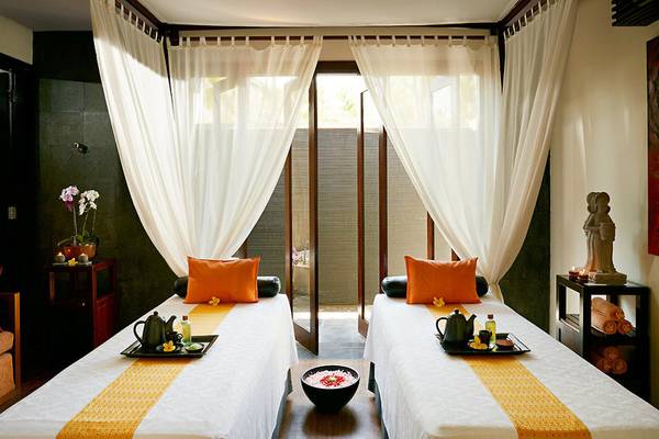 Zwei Betten im Melia Bali Spa mit weißen Laken, gelben Tischdecken und orangen Kissen.