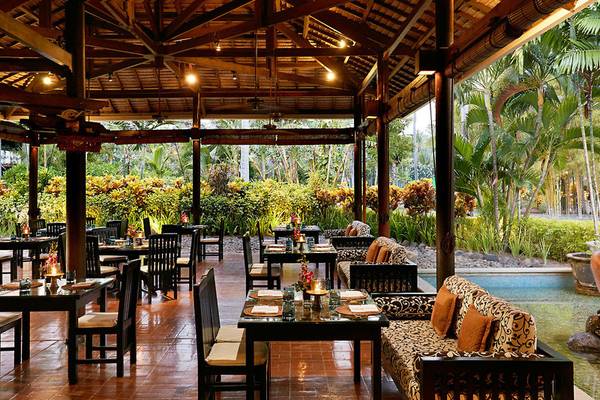 Außenbereich des Restaurants im Melia Bali Hotel mit Tischen und Stühlen, beleuchtet und mit Blick auf den Pool.