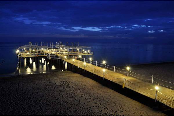 Beleuchteter Pier des Susesi Luxury Resort bei Nacht mit Blick auf das Meer.