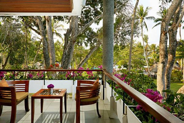 Der Balkon des Melia Bali Hotels mit Tisch und Sesseln, umgeben von Pflanzen und Bäumen.