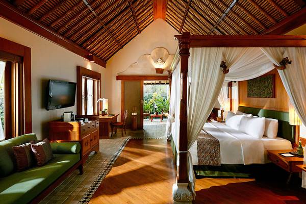 Luxuriöses Zimmer im Melia Bali Hotel mit vierpfostenbett, grünem Sofa und Fernseher.