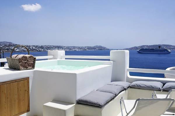 Balkon des Rocabella Mykonos Art Hotel & Spa mit Whirlpool und Blick auf das Meer und eine Kreuzfahrt.