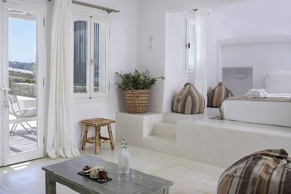 Inneneinrichtung des Rocabella Mykonos Art Hotel mit weißen Wänden, einem Bett, einem Tisch und einem Korb mit einer Pflanze.