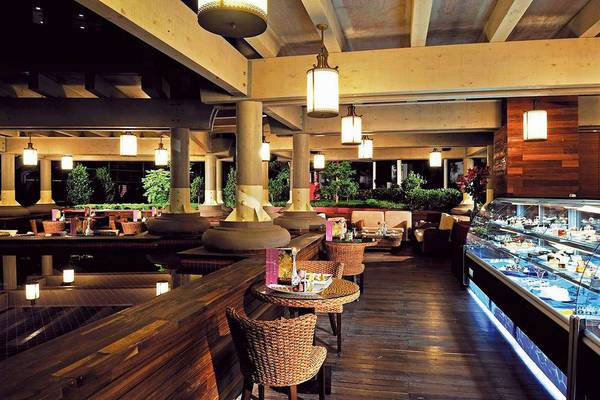 Innenansicht des Restaurants im Susesi Luxury Resort mit Holzmöbeln, hängenden Lampen und einer Theke mit Desserts.