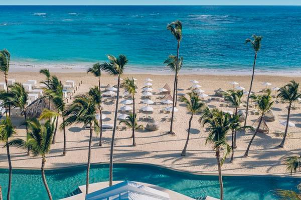 Luftaufnahme des Coral Level at Iberostar Selection Bávaro Strandes mit Palmen, weißen Sonnenschirmen und einem blauen Meer.