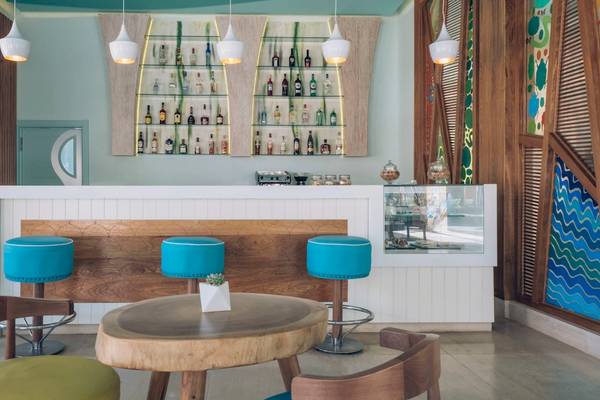 Innenansicht der Bar im Coral Level at Iberostar Selection Bávaro Hotel mit blauen Stühlen und Holztisch.