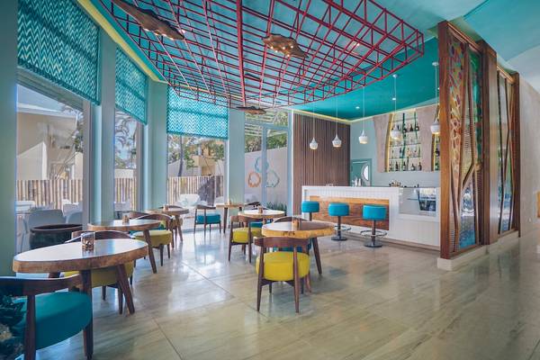 Innenansicht des Coral Level at Iberostar Selection Bávaro mit blauen und roten Akzenten, Holztischen und Stühlen.