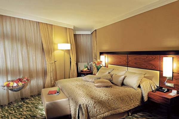 Ein elegantes Hotelzimmer im Susesi Luxury Resort mit einem großen Bett, Kissen, Tischlampen und einem Tisch mit Telefon und Notizbuch.